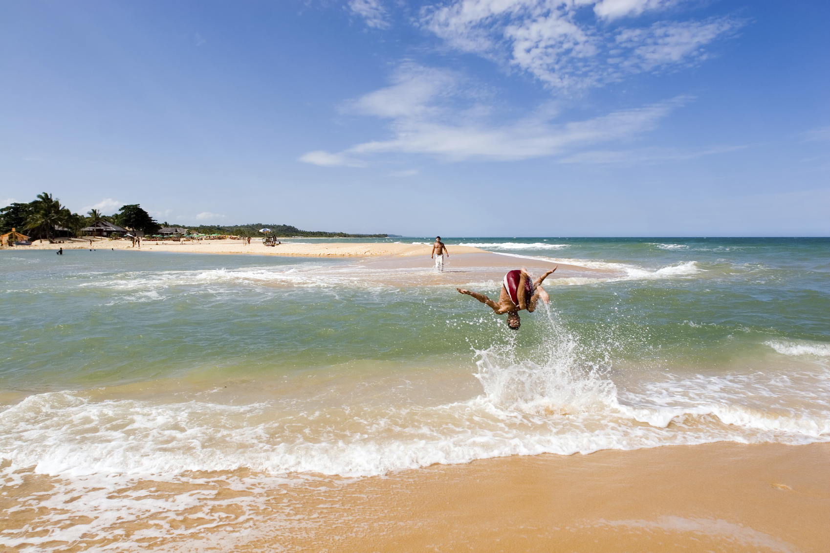 healthy young man in action having fun, playing and somersalting on a acrobat fashion, upside down, on the waters of a green river that meets the sea in a beautiful and sunny tropical beach